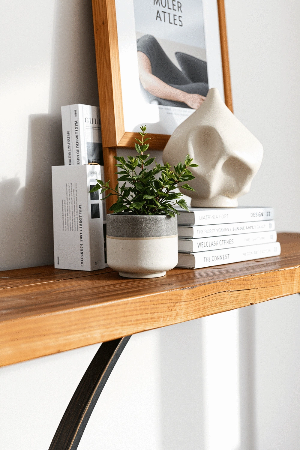 Close-up of a rustic wooden console table with a ceramic pot holding a small green plant, a stack of design books, and a unique sculptural art object.